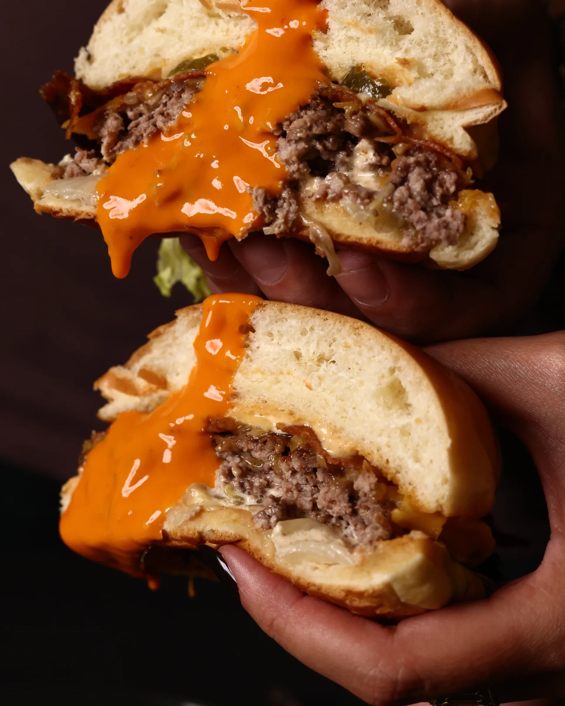 Hot sauce pouring over a smash burger held in one hand